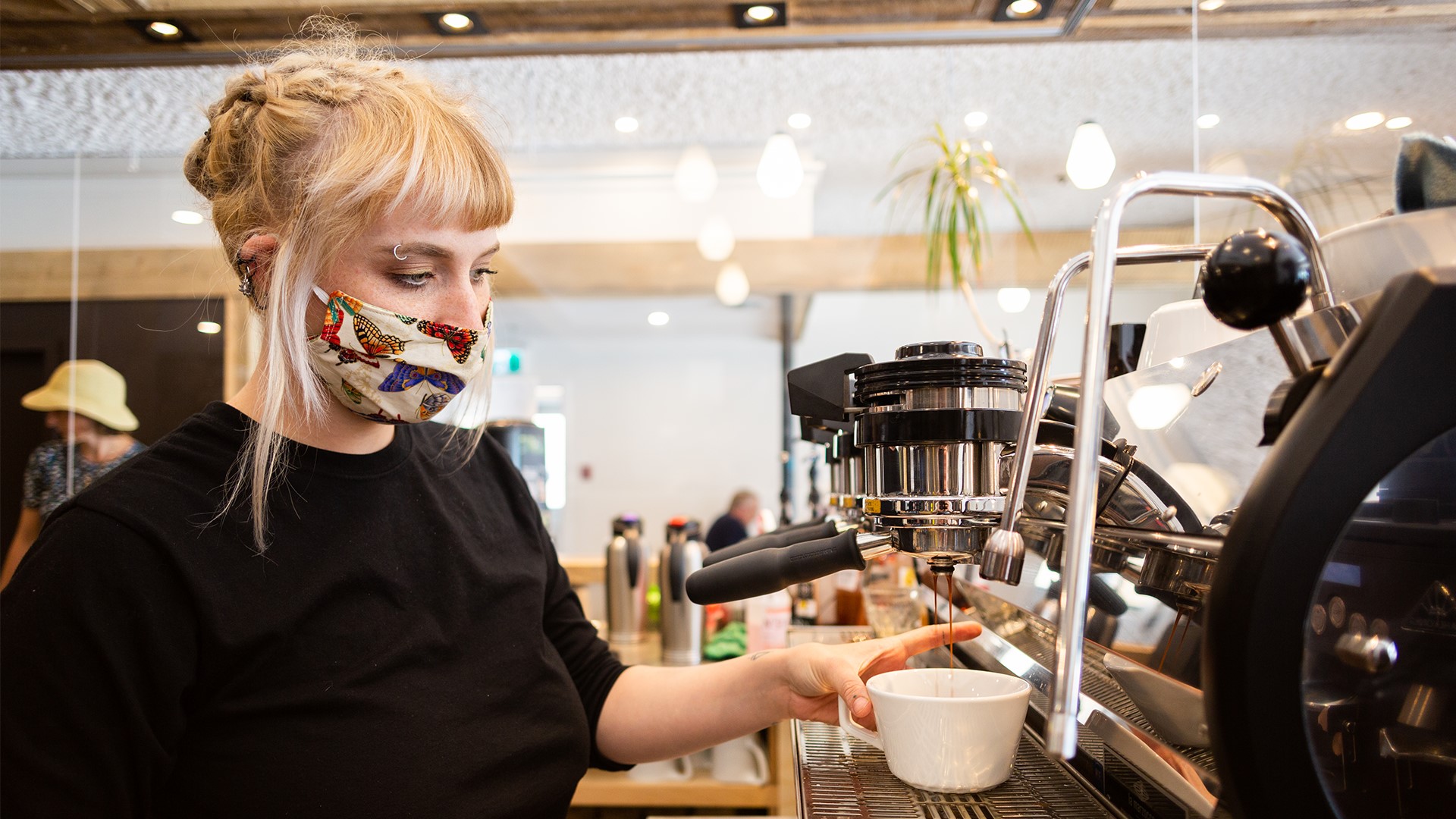 woman in mask preparing cup of coffee