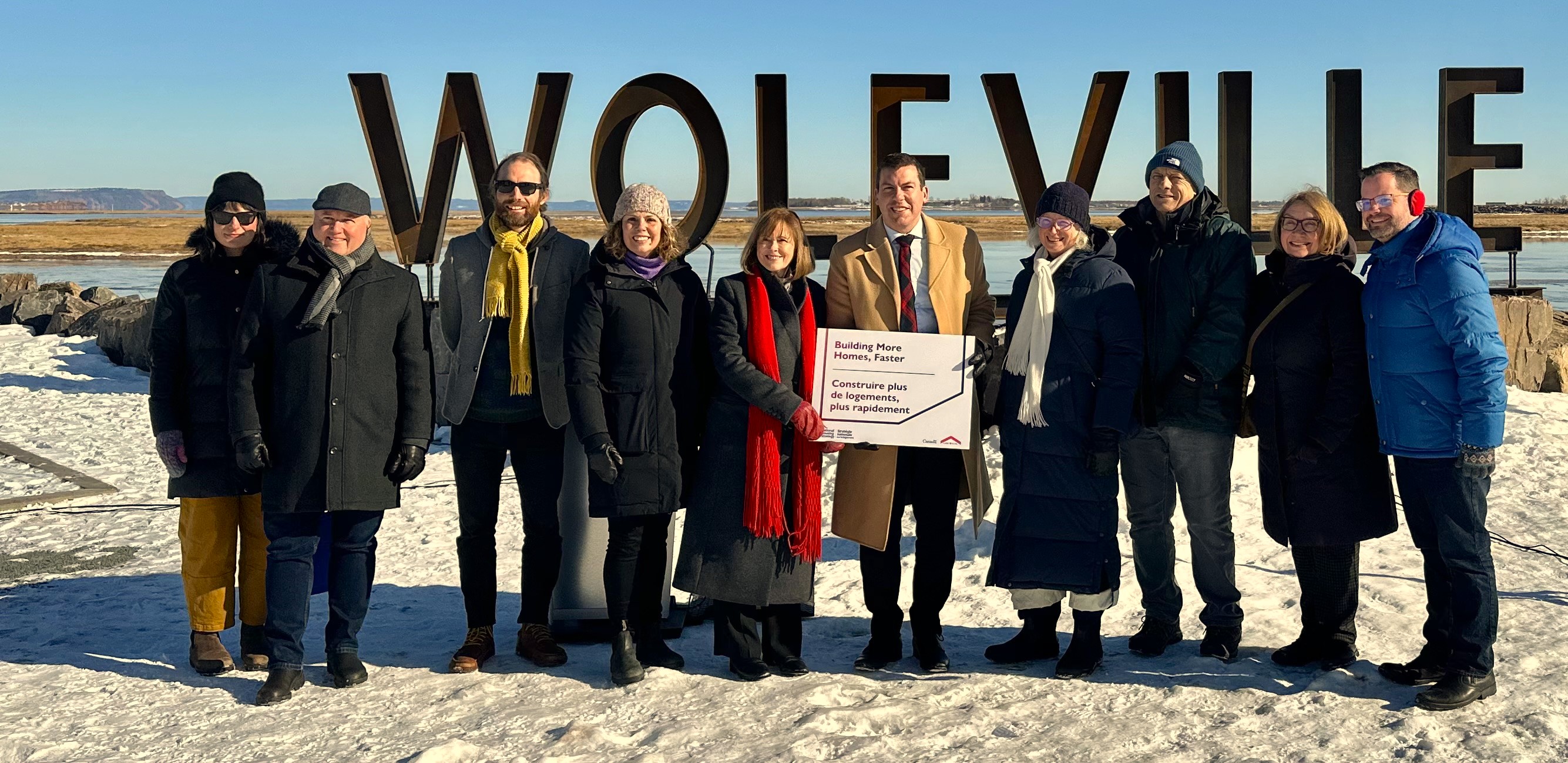 A crowd stands in front of the Wolfville sign.
