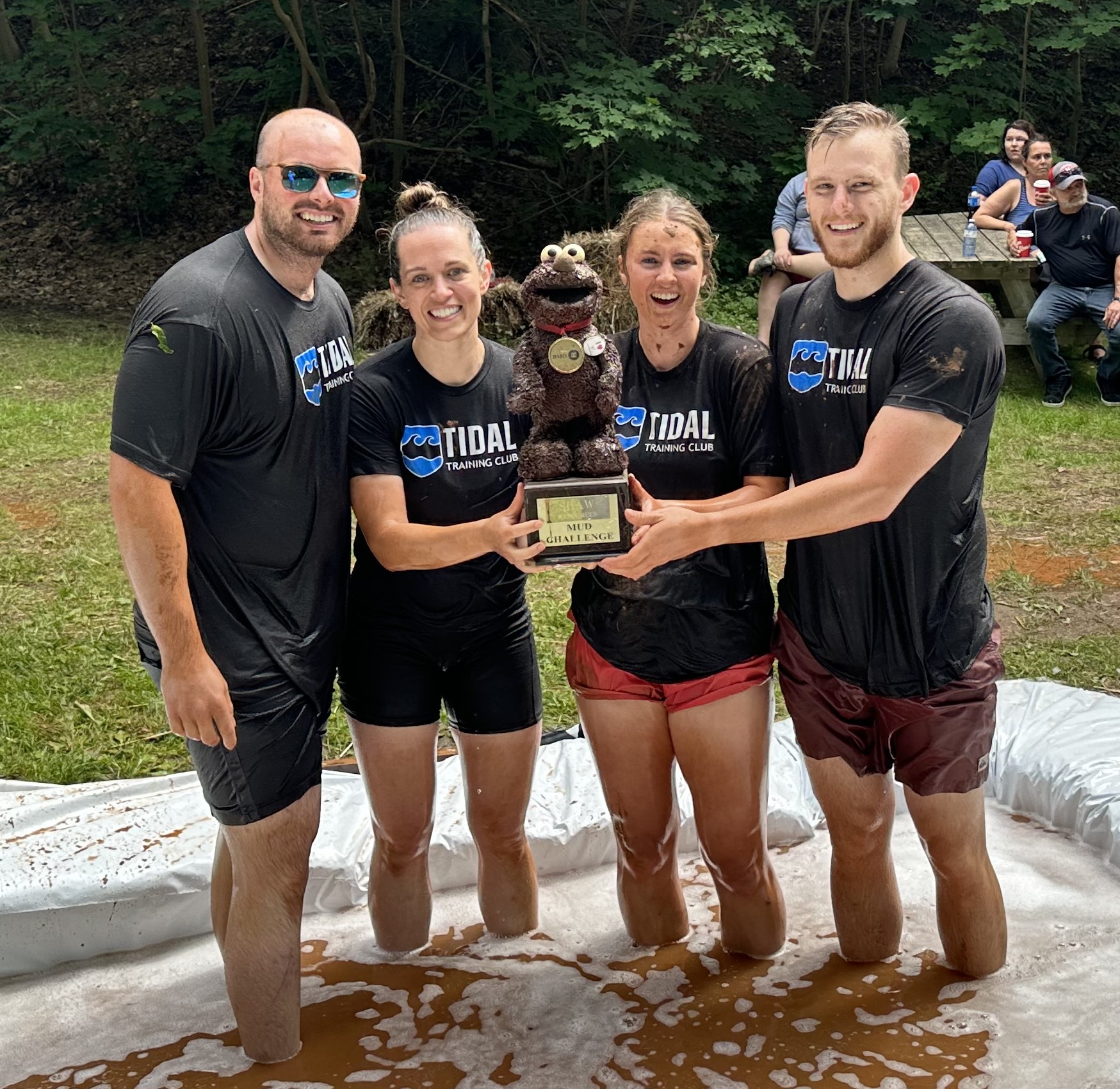 Four wet people smile while holding the Mud Challenge trophy for 2023