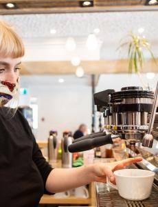 woman in mask preparing cup of coffee
