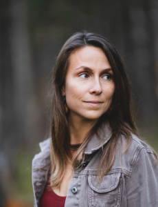 Kristen Martell: a mid-thirties white woman with brown hear wearing a grey button-up and red top looks off to the right of the camera