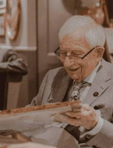 A photo of an older man opening a gift. 