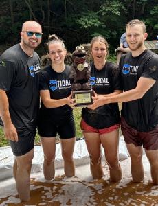 Four wet people smile while holding the Mud Challenge trophy for 2023