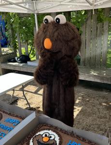 Exited Mudley the mascot is standing in front of two birthday cakes